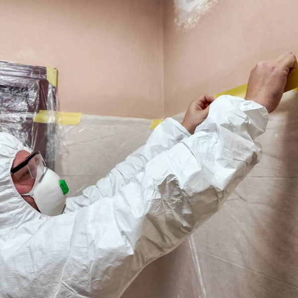 Painter wearing a paint suit and paint mask using paint supplies, like tape, to prep the space near Central Tennessee!